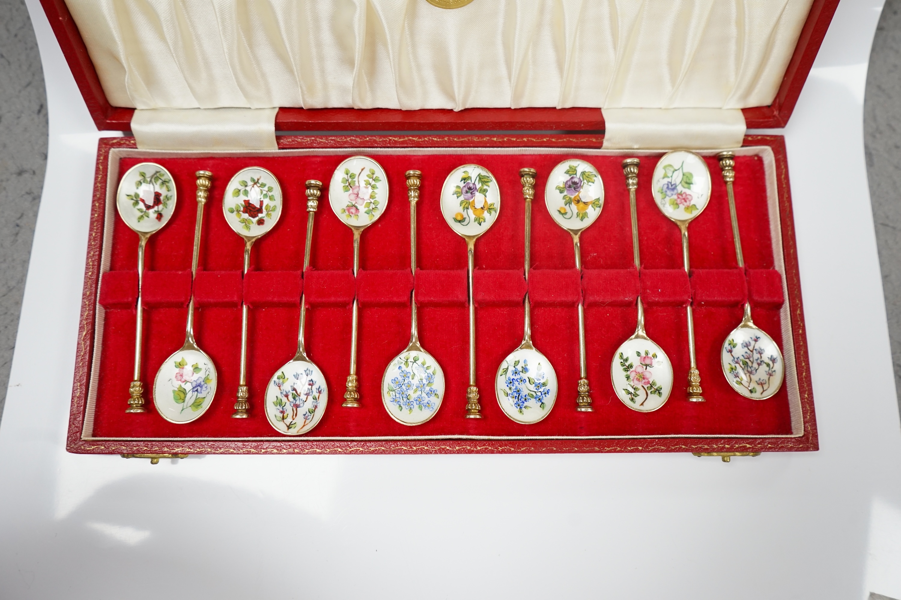 A cased set of twelve early 1970's silver gilt and enamel coffee spoons, decorated with flowers, S.J. Rose & Son, Birmingham, 1971, 98mm. Condition - fair to good